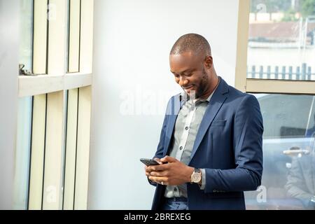 young african business man wearing a suit smiling and using his mobile phone in the office Stock Photo