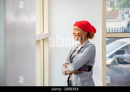young african business woman wearing a suit smiling and looking out the window in her office Stock Photo