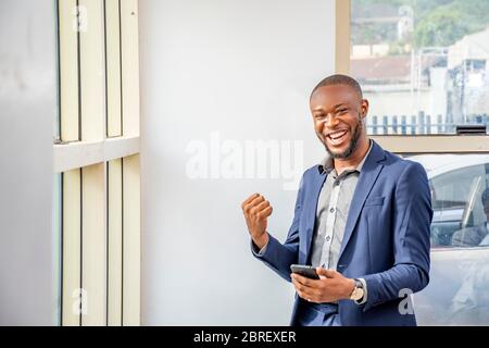 young african businessman feeling excited and happy celebrating while holding his mobile phone Stock Photo