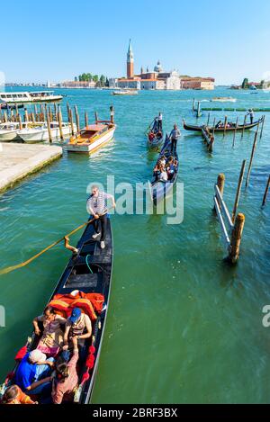 Venice, Italy - May 18, 2017: The gondolas with tourists are sailing along a canal. Gondola is the most attractive tourist transport in Venice. Stock Photo