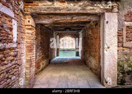 Exit to the water canal from courtyard, Venice, Italy. Vintage corridor of yard of residential area. Ancient architecture of Venice. Old street of the Stock Photo