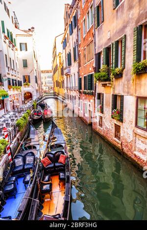 Street with moored gondolas and cafe, Venice, Italy. Scenic view of the Venice canal in summer. Colorful vintage houses of Venice with flowers. Romant Stock Photo