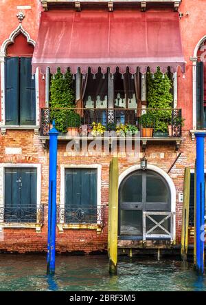 Old red facade in Venice, Italy. Front view of the building exterior with entrance in Venice. Vintage hotel or residential house on the water. Ancient Stock Photo