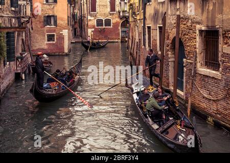 Venice, Italy - May 20, 2017:  Gondolas with tourists floats along the old narrow street. Gondola is the most attractive tourist transport in Venice. Stock Photo