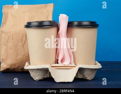 brown paper disposable cups with a plastic lid stand in the tray on a blue wooden table, takeaway containers Stock Photo