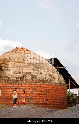 Two young Cambodian girls play together outside a beehive brick kiln. Battambang, Cambodia, Southeast Asia Stock Photo
