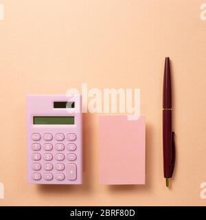 Work and study place, memo pad and digital calculator and pen on beige pink background. flat lay, top view, copy space Stock Photo