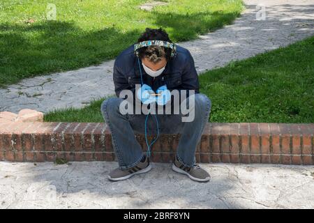 Campobasso,Molise region,Italy:A boy, chatting and listening to music with his mobile phone, sitting in a city park on days emergency coronavirus in I Stock Photo