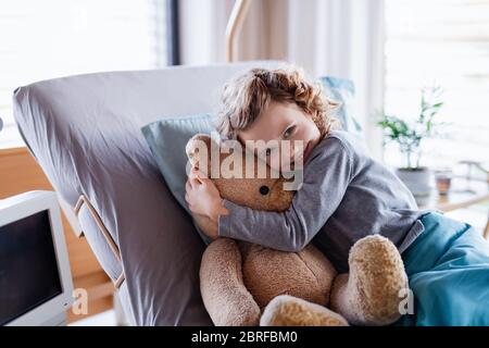 Smiling small girl with teddy bear in bed in hospital.
