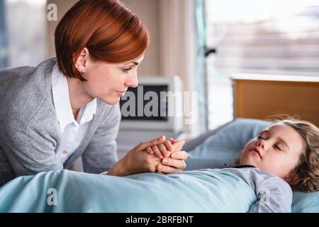 Caring mother visiting small girl daughter in bed in hospital.