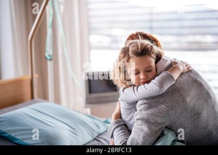 Caring mother visiting small girl daughter in hospital, hugging. Stock Photo