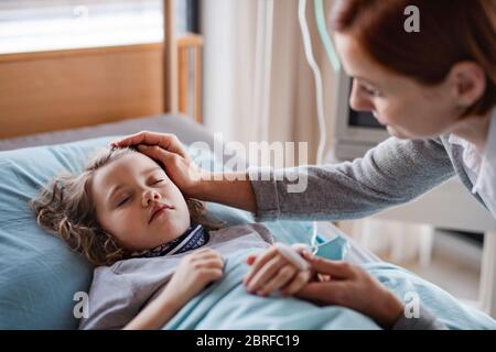 Caring mother visiting small girl daughter in bed in hospital.