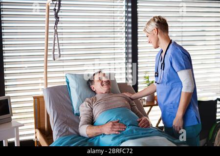 Healthcare worker or nurse tallking to senior patient in bed in hospital. Stock Photo