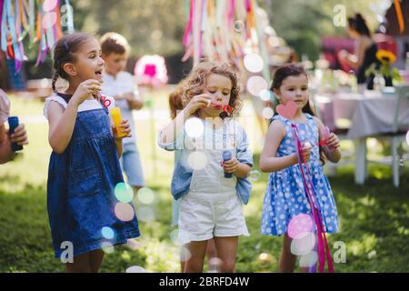 Small children outdoors in garden in summer, playing with bubbles. Stock Photo