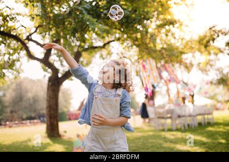 Portrait of small girl playing with bubbles outdoors on garden party in summer. Stock Photo