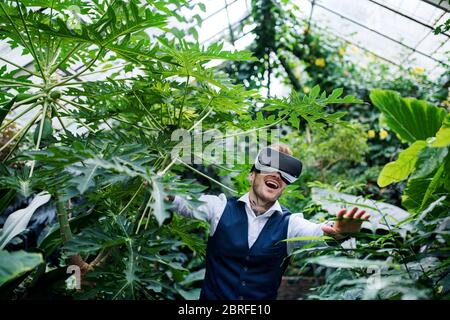 Front view of young man standing in botanical garden, using VR glasses. Stock Photo