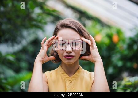 Tired young woman standing in greenhouse in botanical garden. Stock Photo