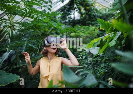 Front view of young woman standing in botanical garden, using VR glasses. Stock Photo