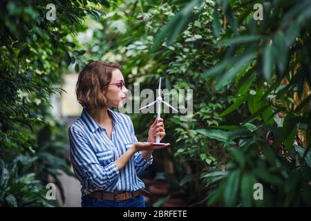 Young woman standing in botanical garden, holding windmill model. Stock Photo