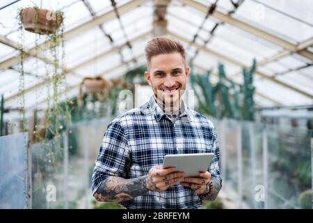 Man researcher standing in greenhouse, using tablet. Stock Photo