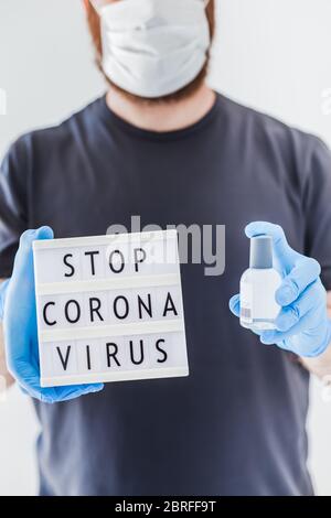Hand sanitizer hygiene alcohol gel bottles and lightbox with text Stop Coronavirus in hands of man wearing latex medical gloves and protective mask du Stock Photo