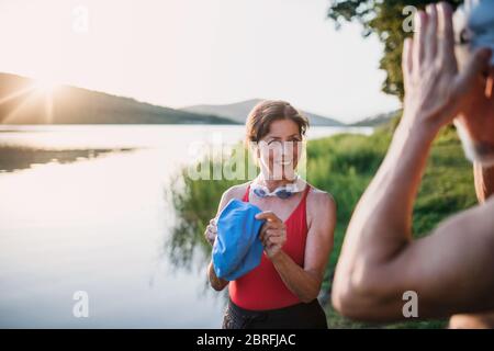 Senior couple in swimsuit standing by lake outdoors before swimming. Stock Photo