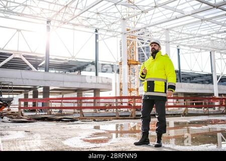 Man engineer standing on construction site, using smartphone. Stock Photo