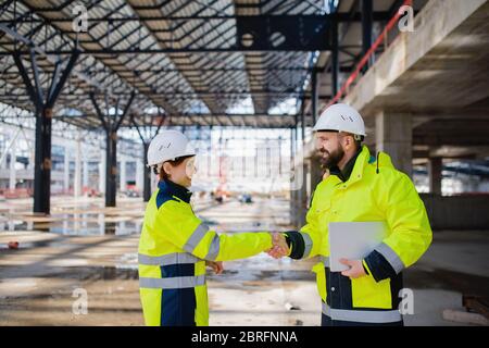Engineers with tablet standing on construction site, shaking hands. Stock Photo