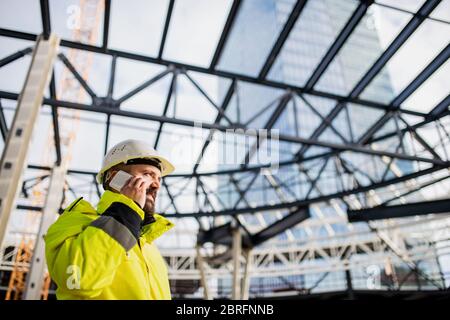Man engineer standing on construction site, using smartphone. Stock Photo