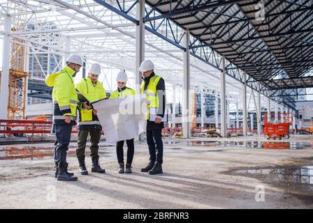 Group of engineers with blueprints standing on construction site. Stock Photo