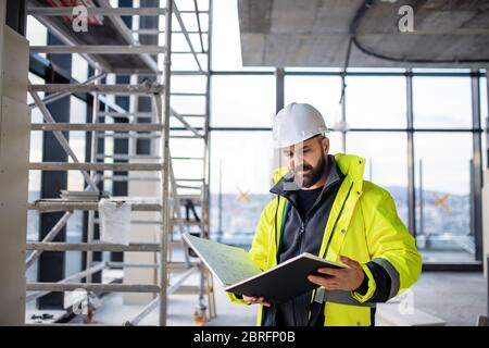 Man engineer standing on construction site, holding blueprints. Stock Photo