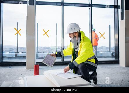 Man engineer with tablet on construction site, looking at blueprints. Stock Photo