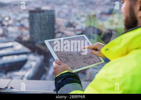Midsection of man engineer with tablet on construction site, looking at blueprints. Stock Photo