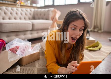 Long-haired girl in a mustard color blouse buying something on internet and looking surprised Stock Photo