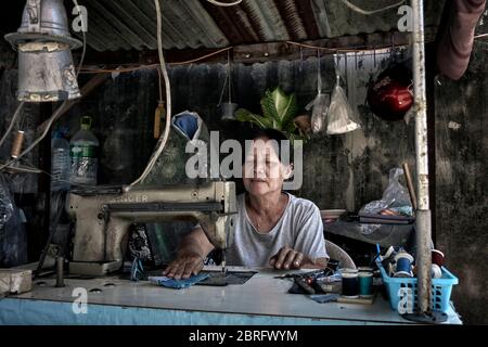 Woman working. Thailand Seamstress working at her back street stall using a vintage sewing machine. Southeast Asia Stock Photo