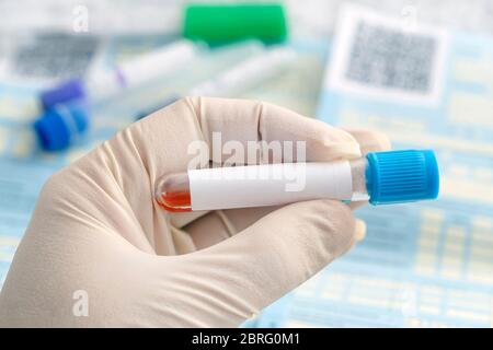 Hand with medical glove of scientist or doctor holds test tube with blood sample and blank label for own text on background of table with medical Stock Photo