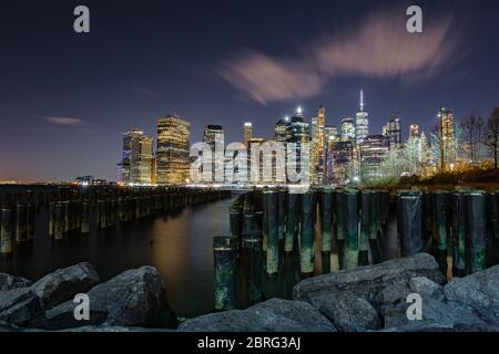 A long exposure of the Manhattan financial district taken from Brooklyn Bridge Park with the poles in the water, New York, USA Stock Photo