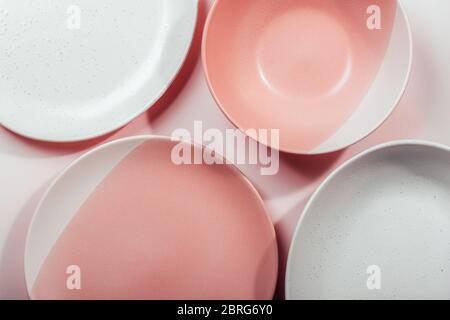 Different porcelain empty plates on a pink background. Multi-colored ceramic handmade dishes. Top view. Stock Photo