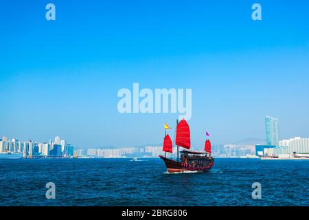 Tourist traditional style cruise sailboat with red sails crosses Victoria harbor from Kowloon to the Hong Kong Island Stock Photo