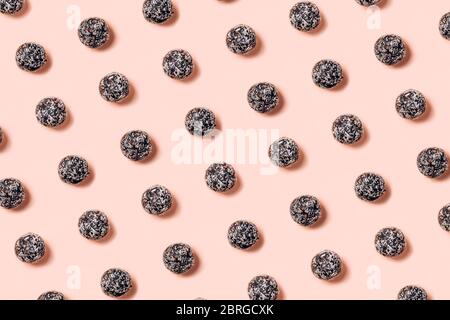 Healthy raw energy balls made of dried fruits and nuts with coconut chips, flax seeds, pistachios, sesame. Pattern on pink background. Stock Photo