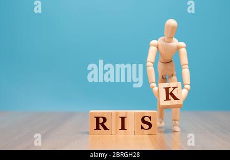 Wooden puppet standing and holding a wooden cube with risk word.  Concept of assessment and analysis on business crisis and investment control on risk Stock Photo