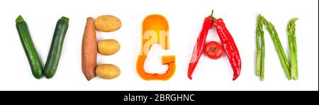 The lettering vegan arranged with different colorful vegetables on white: zucchini, potatoes, butternut squash, red peppers and asparagus. Concept stu Stock Photo