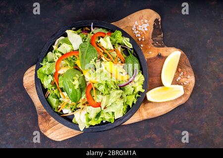 Green salad with vegetables and greens on wooden table with slices of lemon and salt. Fresh salad. Stock Photo