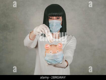woman wearing medical mask for coronavirus with a piggybank over gray background Stock Photo