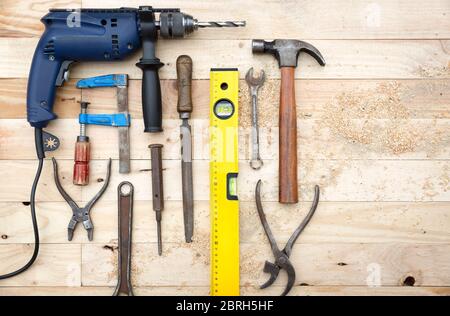 Top view set of tools consisting of drill, hammer and other joinery accessories placed on natural pine wood workbench. Work and DIY concept. Stock Photo