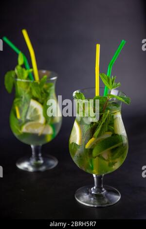 Summer mint lime refreshing cocktail mojito with rum and ice in glass on black background. Mojito cocktail on dark stone table. Glassy high glass for Stock Photo