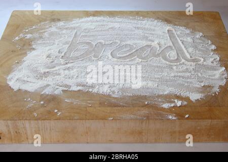 The word bread written in flour on chopping board, writing in flour bread Stock Photo