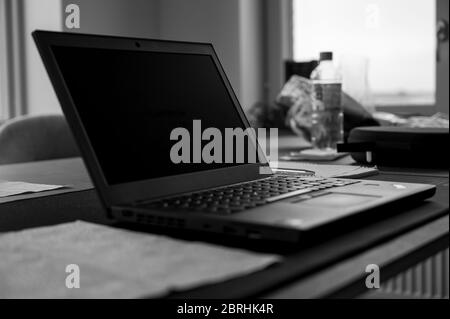 A black and white photo of a turned-off laptop placed on a kitchen table in a realistic home setting, showing the concept of working from home during