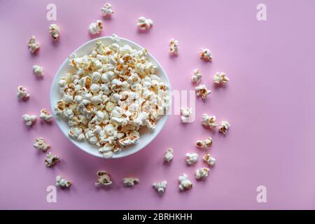 Tasty salted popcorn in white bowl on a pink background and spilled popcorn without a plate on the desk. Home made food concept Stock Photo