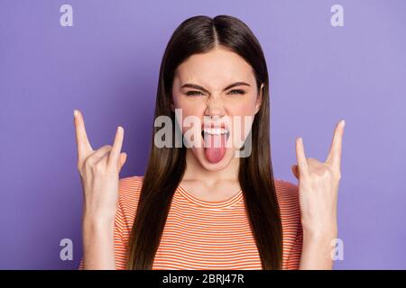 Closeup photo of attractive crazy funky lady long brown straight hairstyle show finger horns sticking tongue wear casual orange striped t-shirt Stock Photo